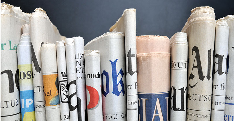 Pressefreiheit: Ein Stapel unterschiedlicher Zeitungen nebeneinander auf grauem Hintergrund
