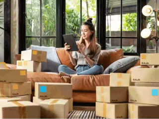 Eine Frau sitzt mit einem Tablet auf dem Sofa, umringt von Paketen.